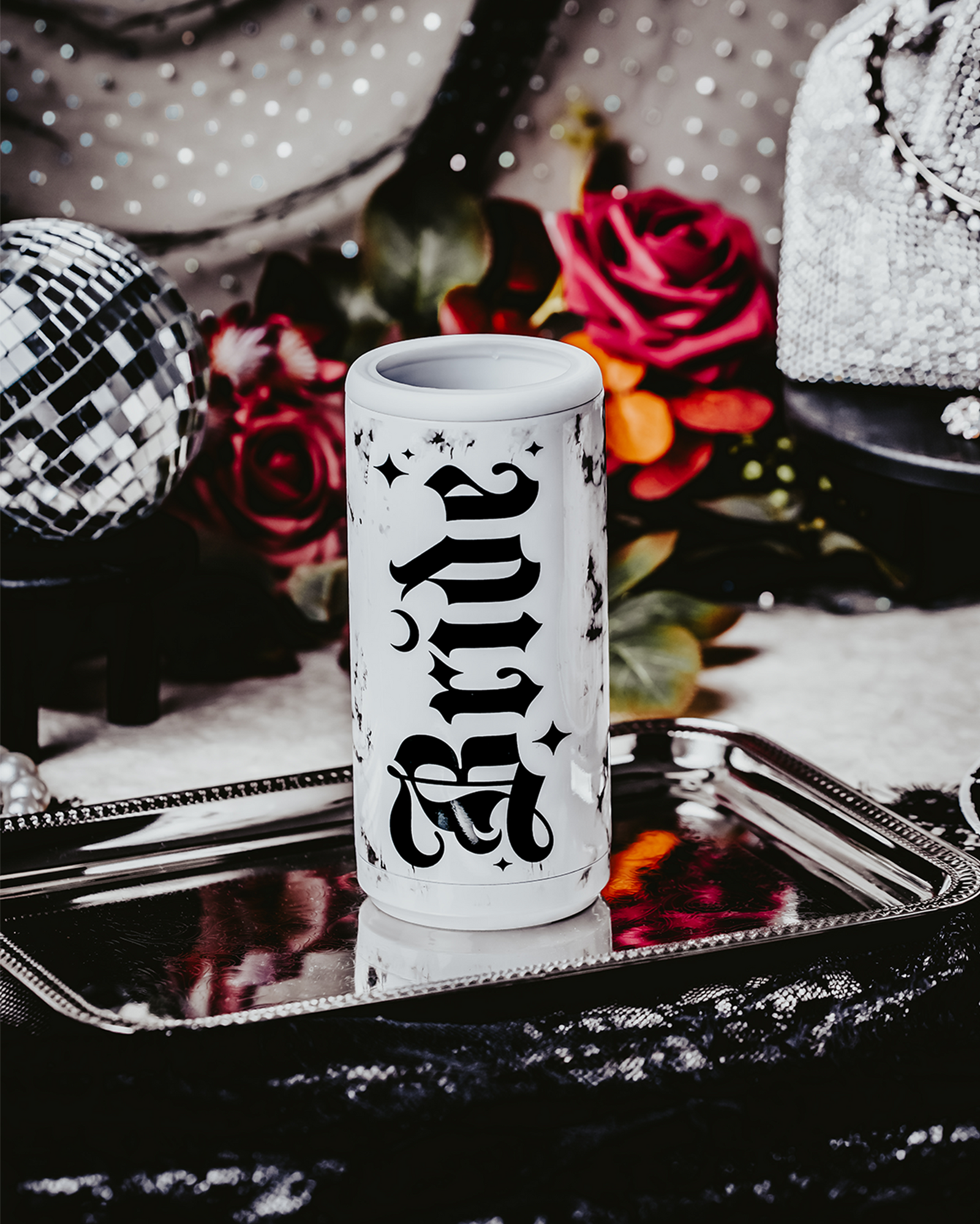 Set of three white, marble-patterned skinny can coolers with gothic black lettering. One cooler reads 'Bride,' and the other two read 'Bride's Coven,' all set against a dark, moody background with lace, disco balls, and red roses, creating a gothic and alternative bridal party theme.
