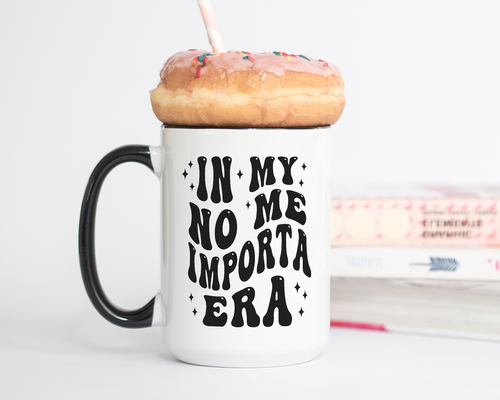 White ceramic mug with a black handle and rim, featuring bold black text that reads "In My No Me Importa Era" in a groovy, retro-style font, surrounded by small decorative sparkles.