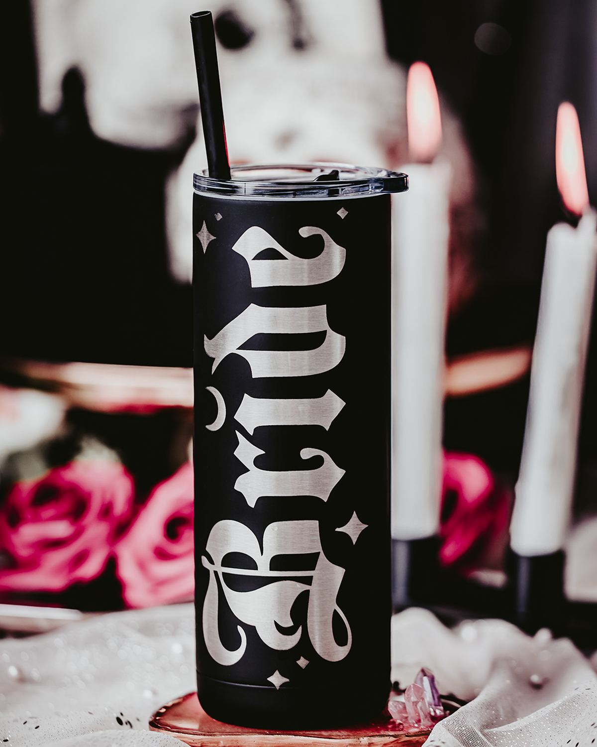 Set of two black stainless steel tumblers, one engraved with &#39;Bride&#39; and the other with &#39;Groom&#39; in bold, gothic silver lettering. Each tumbler features a black straw and is set against a dramatic, gothic backdrop with red roses, lace, and soft, romantic lighting, perfect for an alternative or darkly romantic wedding theme.