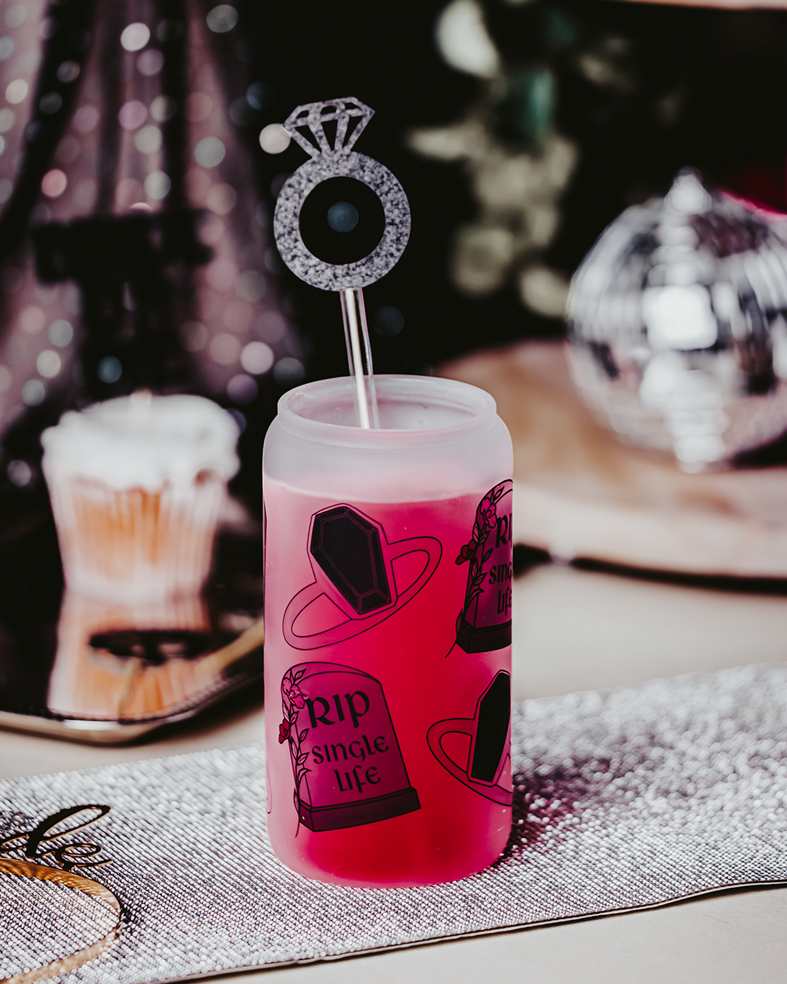 Frosted glass can with a bamboo lid and straw, featuring gothic-themed illustrations of a coffin and tombstone with the phrase 'RIP Single Life.' The can is surrounded by red and white roses, a gold 'Bride' headband, and decorative rings, creating a dark, romantic bridal atmosphere.
