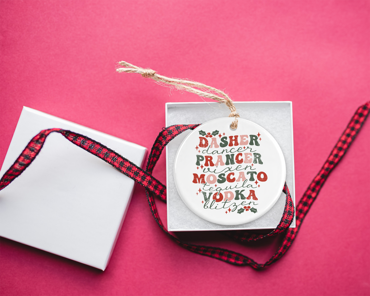 Round ceramic ornament with festive lettering listing reindeer names alongside holiday drinks like “Moscato” and “Vodka,” perfect for adding humor to holiday decor.