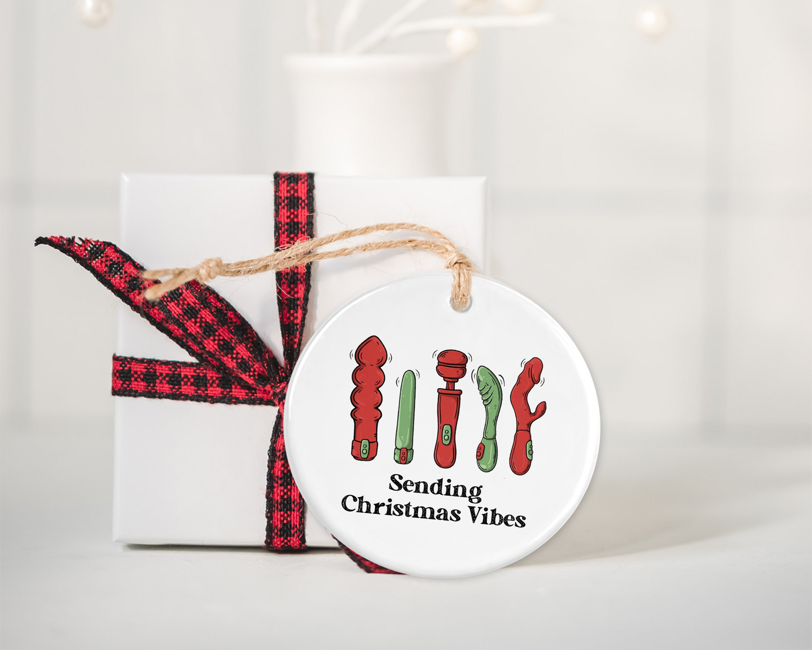 Round ceramic Christmas ornament with a humorous illustration of various adult toy shapes spelling out “Sending Christmas Vibes,” adding a cheeky, playful twist to holiday decor.