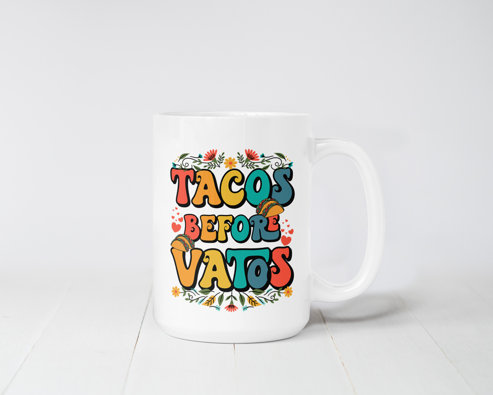 White ceramic mug with bold, colorful “Tacos Before Vatos” text surrounded by floral and taco graphics