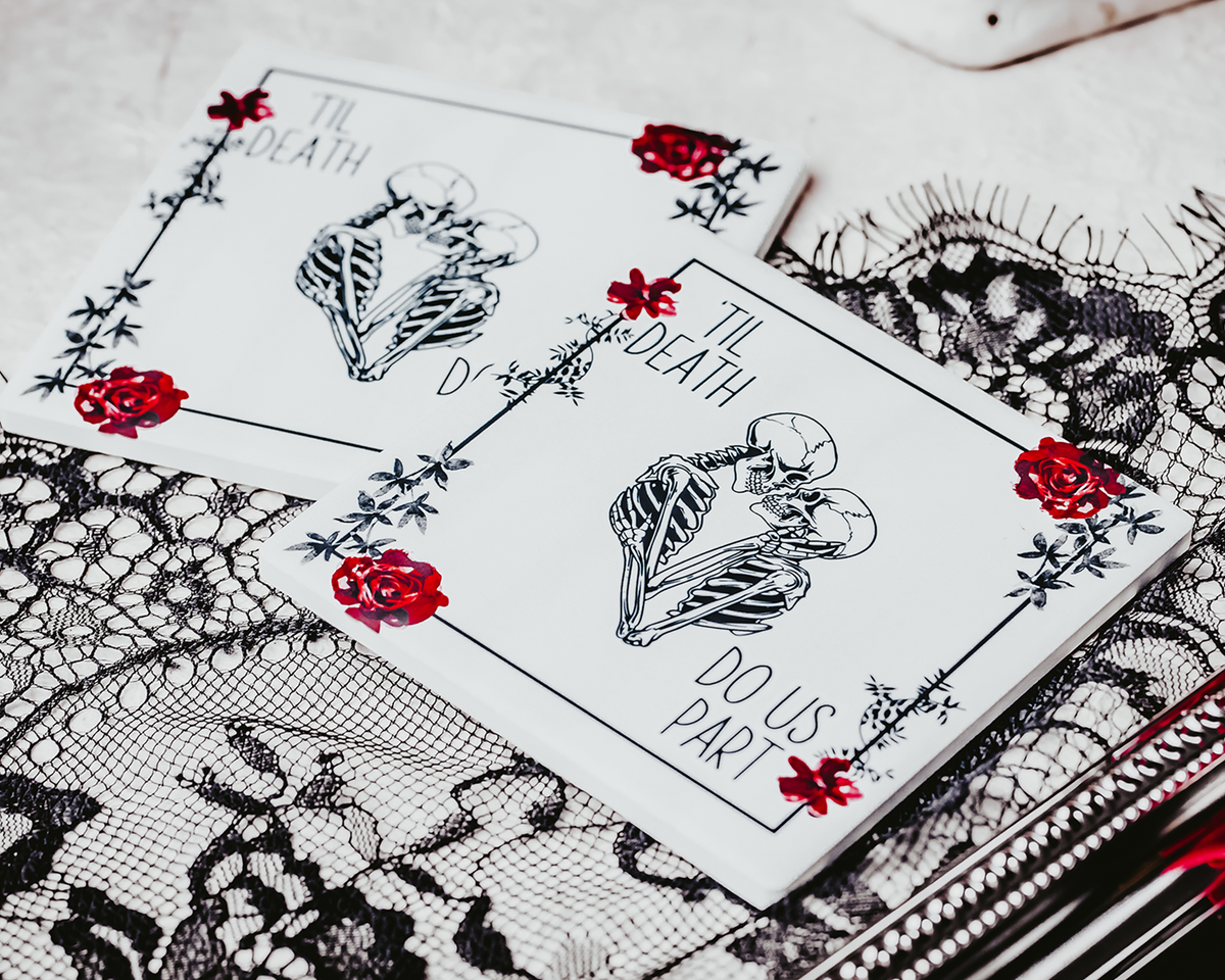 Two square coasters featuring a gothic &#39;Til Death Do Us Part&#39; design with skeletons and red roses, placed on black lace fabric.