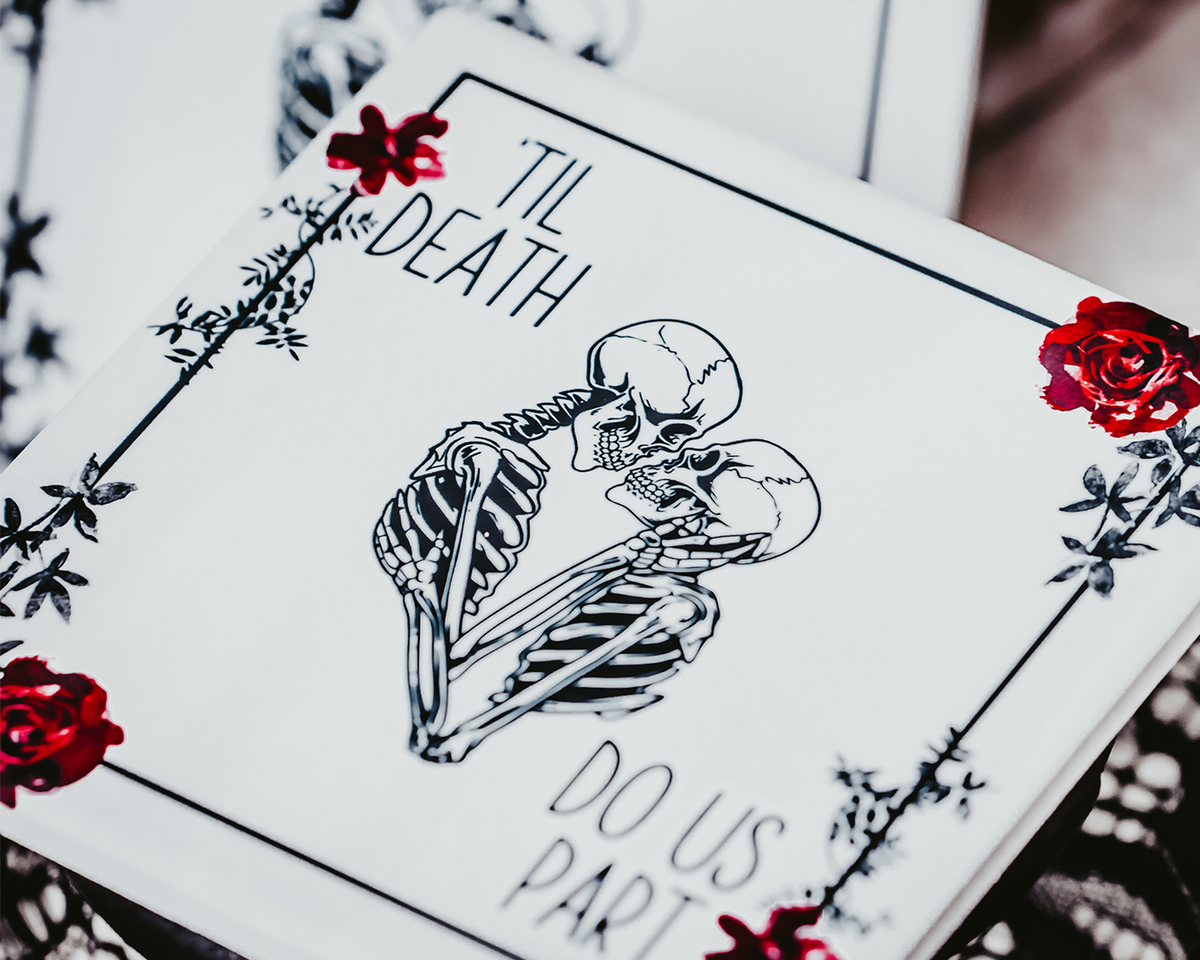 Two square coasters featuring a gothic &#39;Til Death Do Us Part&#39; design with skeletons and red roses, placed on black lace fabric.