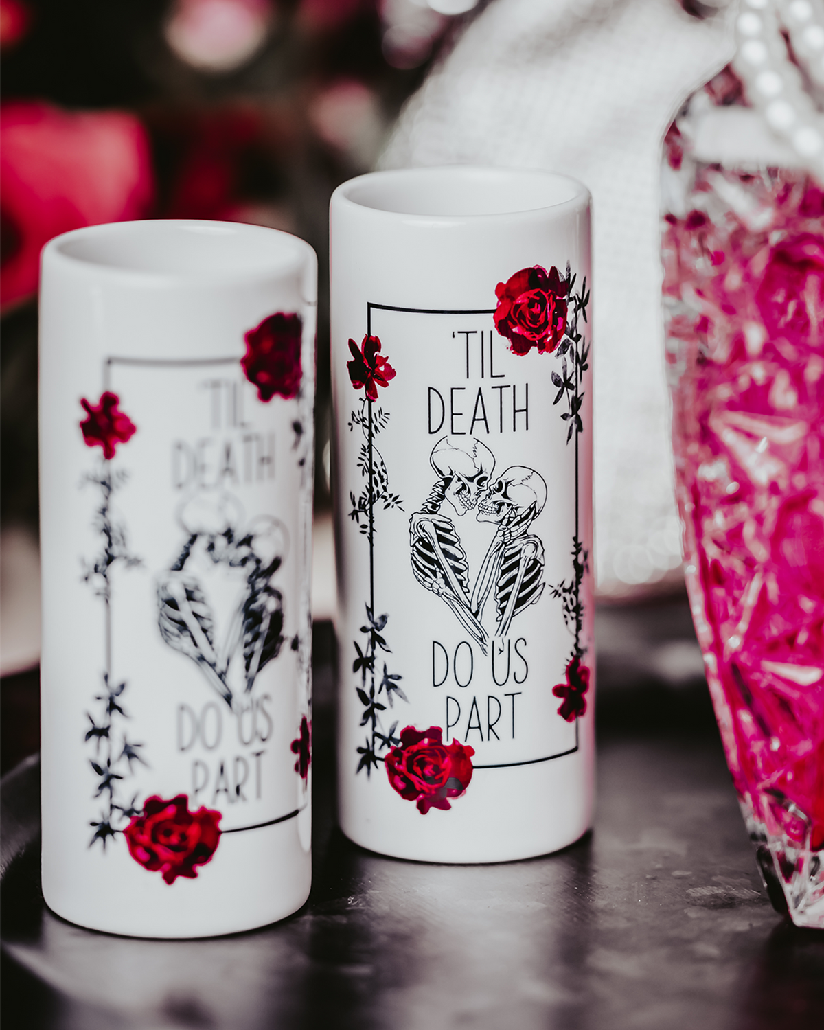 Two white ceramic shot glasses featuring a &#39;Til Death Do Us Part&#39; skeleton design with red roses, perfect for gothic weddings or bridal gifts. Shot glasses are 3oz and showcase a bold, edgy look.